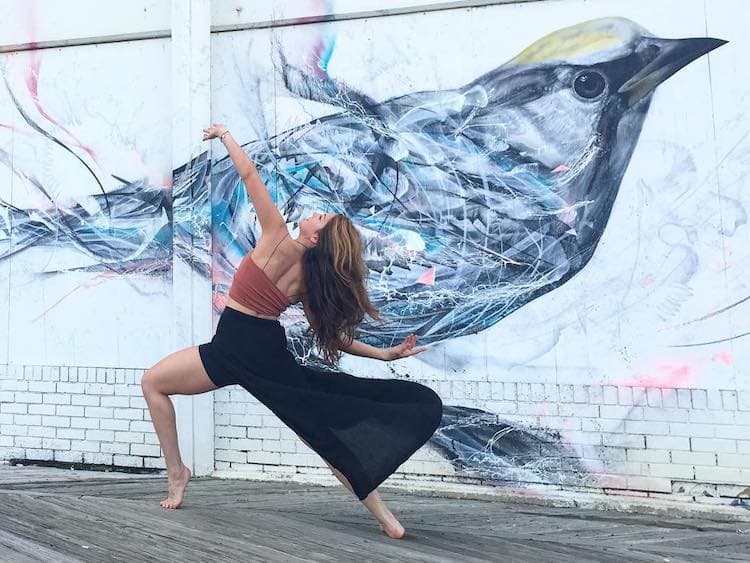 A dancer striking a dramatic pose in front of a large bird mural