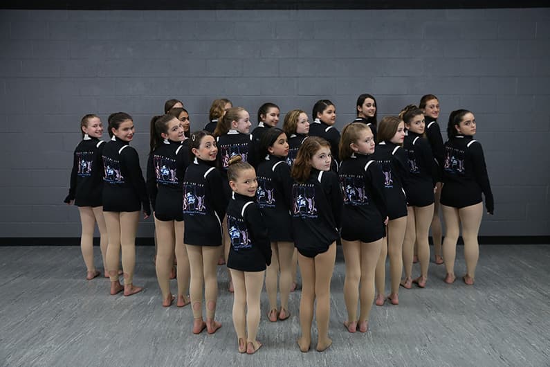 Company dancers lined up in matching Dance For Joy jackets in the studio